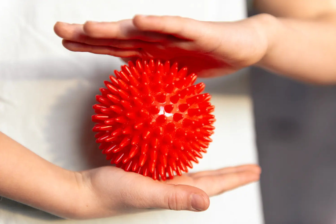 Hands holding a red spiky sensory ball illustrating signs your child needs sensory toys