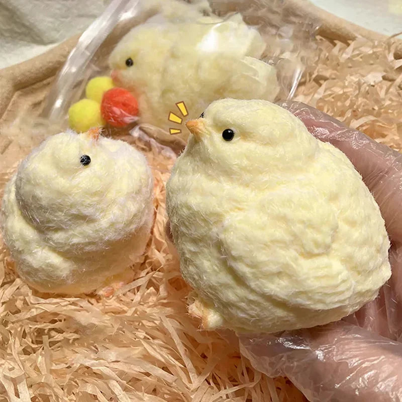 A hand in a plastic glove holds a fluffy yellow chick among many similar chick figures, showcasing their soft texture and round shape.