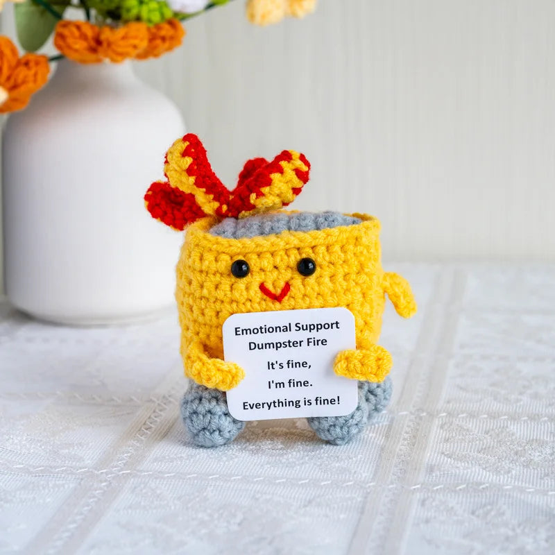 Handmade crochet emotional support buddies in the shape of a cheerful dumpster fire holding a sign