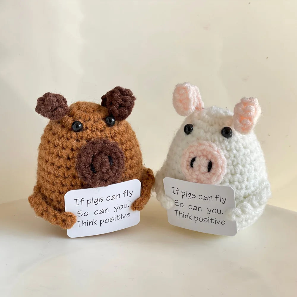 Two handmade crochet emotional support buddies in pig shapes holding motivational signs