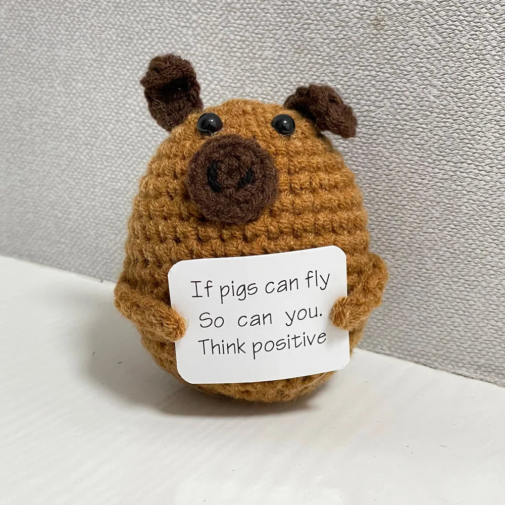 Handmade crochet emotional support buddies in the shape of a pig with an inspiring message on a sign