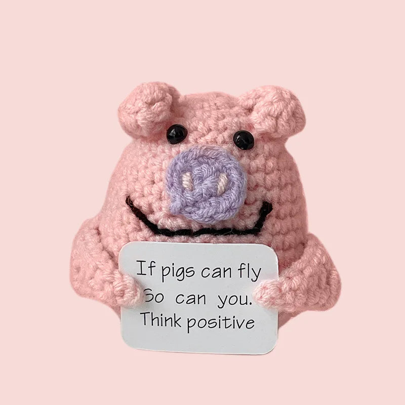 Handmade crochet emotional support buddies in the shape of a pig holding an uplifting message sign