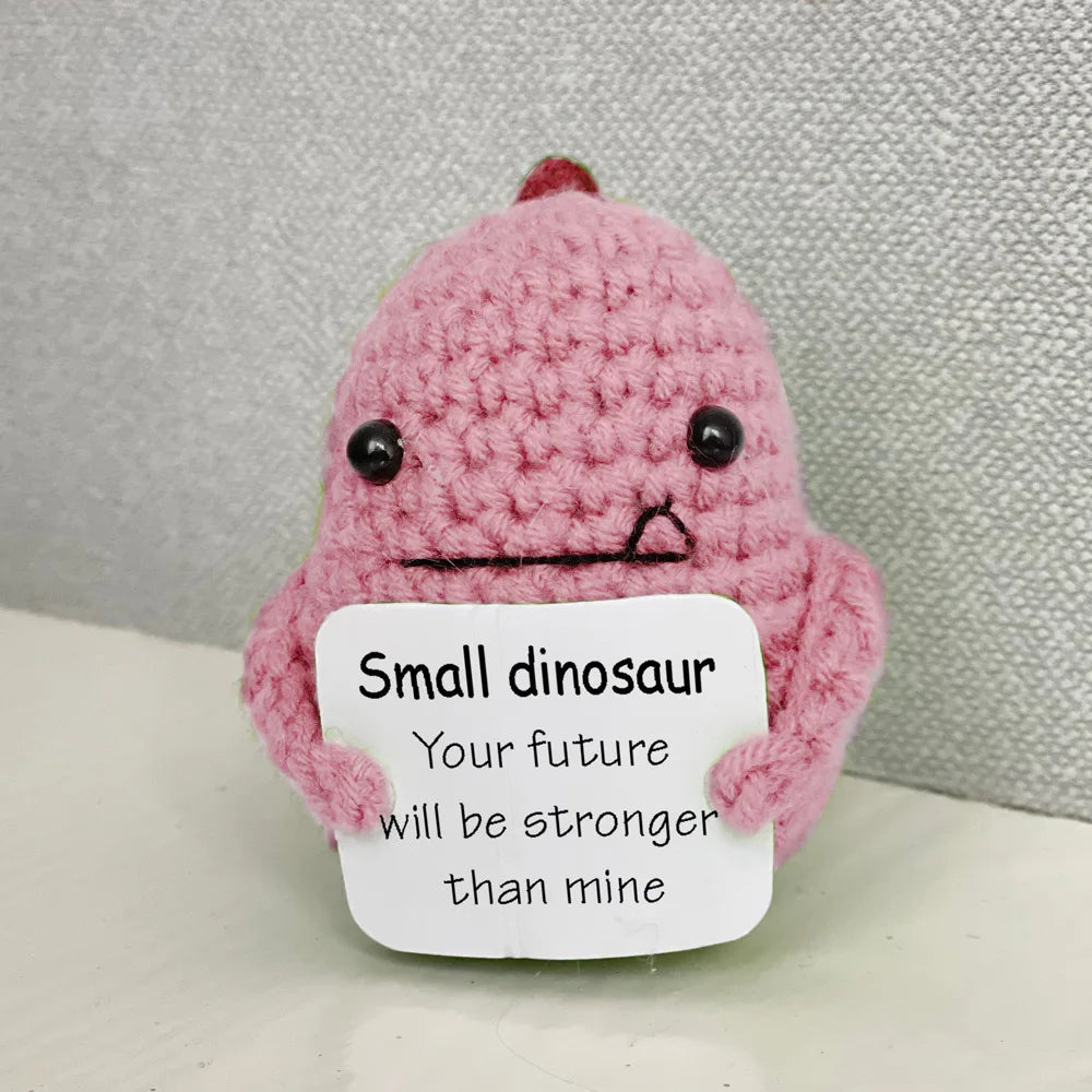 Handmade crochet emotional support buddies in the form of a cute small dinosaur holding an encouraging sign