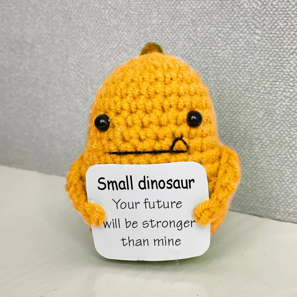 Handmade crochet emotional support buddies in the shape of a small dinosaur holding a motivational sign