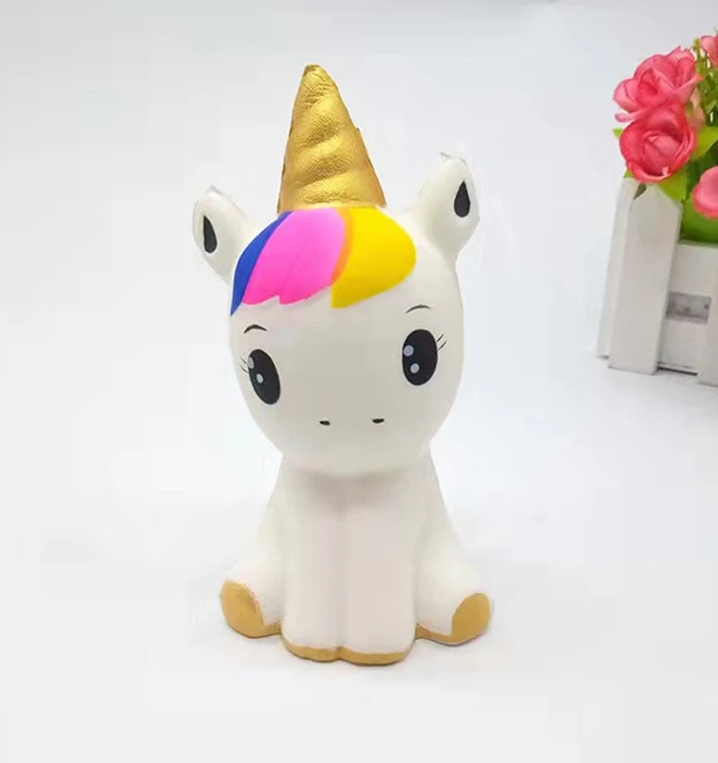 Cute white unicorn figurine with a golden horn and colorful mane, sitting on a plain background with a floral arrangement nearby.