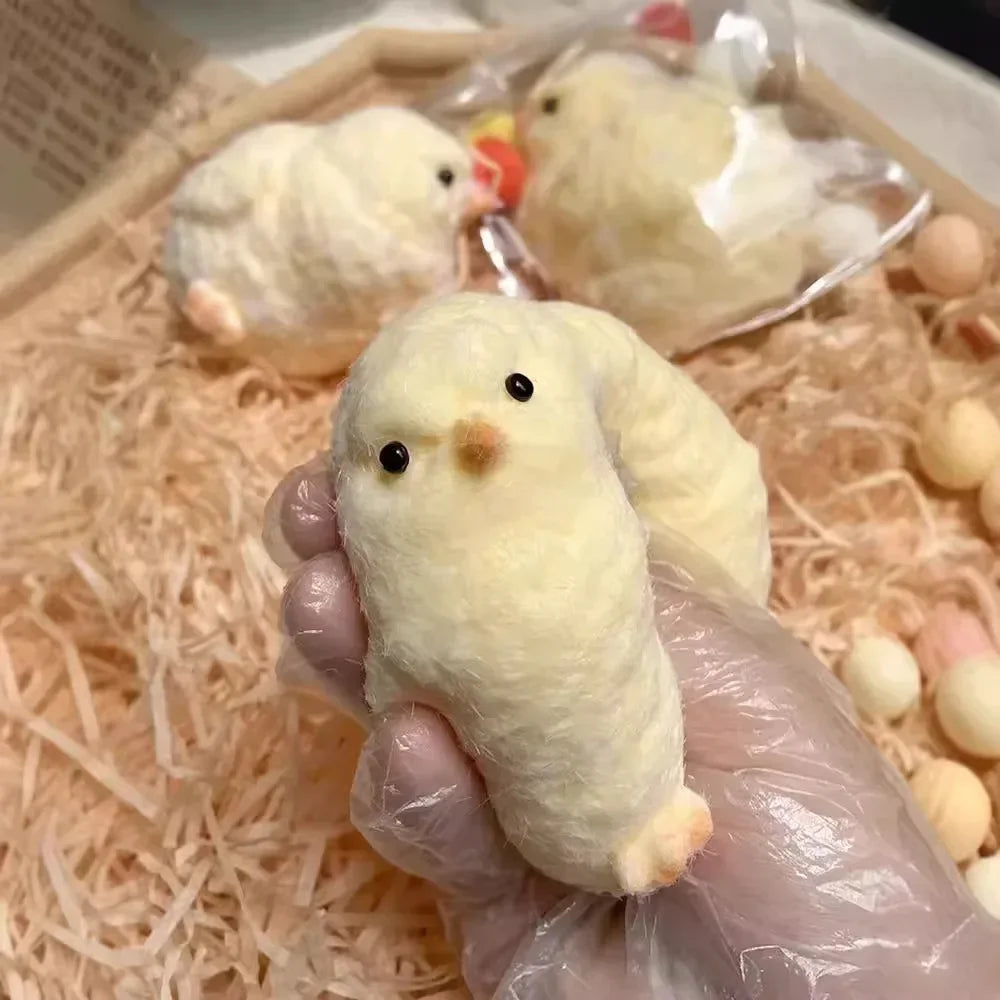 A hand in a plastic glove squishes a fluffy yellow chick among many similar chick figures, showcasing their soft texture and round shape.