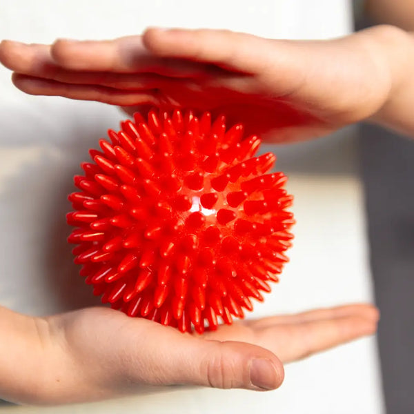 Hands holding a red spiky sensory ball illustrating signs your child needs sensory toys