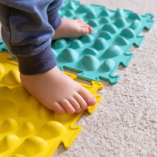 Child's feet on textured yellow and blue tactile mats for sensory play for children with autism