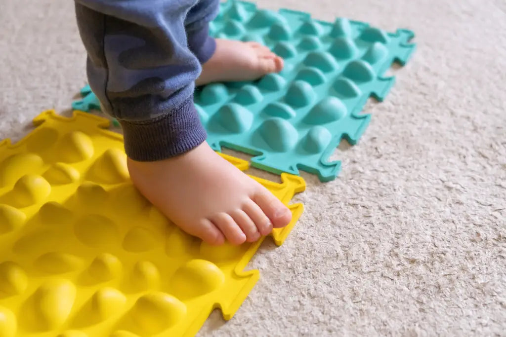 Child's feet on textured yellow and blue tactile mats for sensory play for children with autism