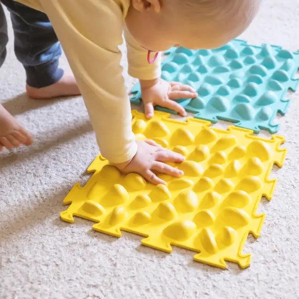 Toddler playing with textured foam mats as sensory games for special needs children on carpeted floor