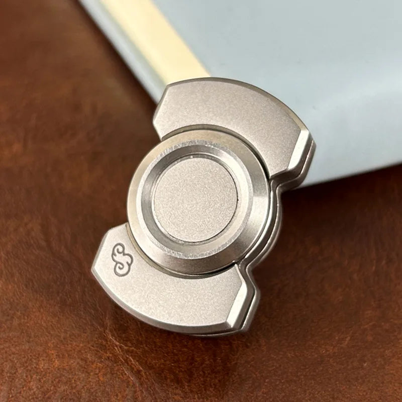 Metal 3 in 1 Fidget Toy for Stress Relief on a leather surface beside a notebook.
