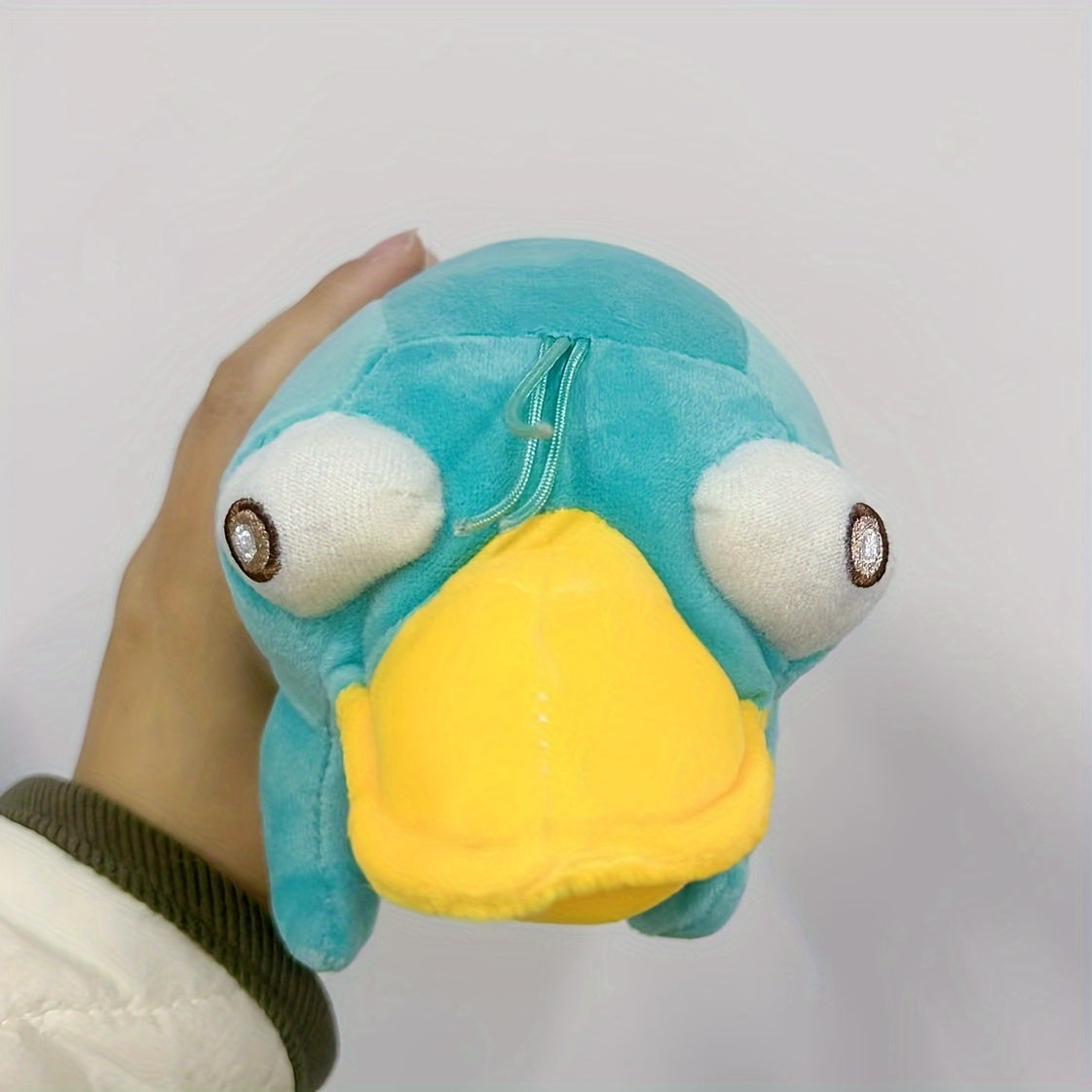 Hand holding a blue platypus plush toy with large eyes and a yellow bill