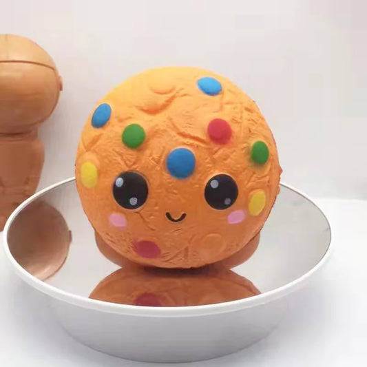 Cookie ball squishy toy in orange with colorful sprinkles and a happy face on a reflective surface