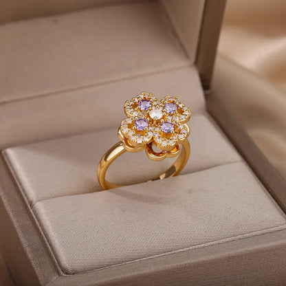 Gold flower-shaped adjustable therapeutic fidget ring with purple and clear stones in a beige jewelry box