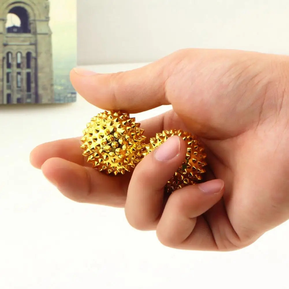 Hand holding two gold magnetic acupoint massage balls with textured surfaces for stress relief