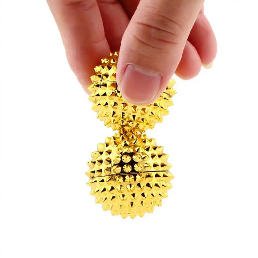 Hand holding a golden magnetic acupoint massage ball with spiked surfaces for relaxation and therapy