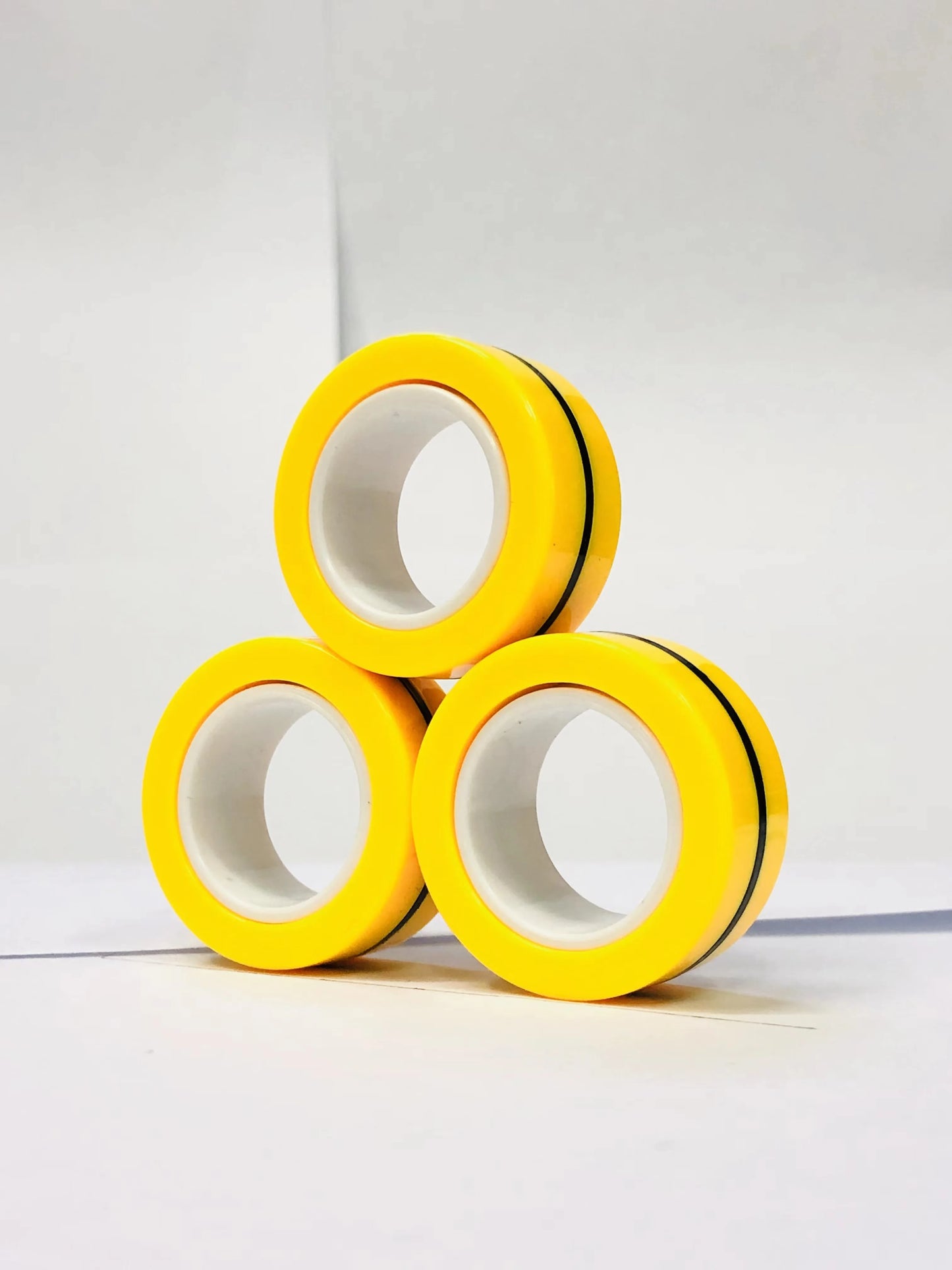 Three yellow magnetic finger ring fidget toys stacked in a triangular formation for stress relief