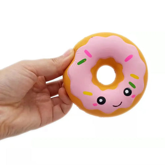 Hand holding a pink frosted donut squishy toy with a smiling face and colorful sprinkles