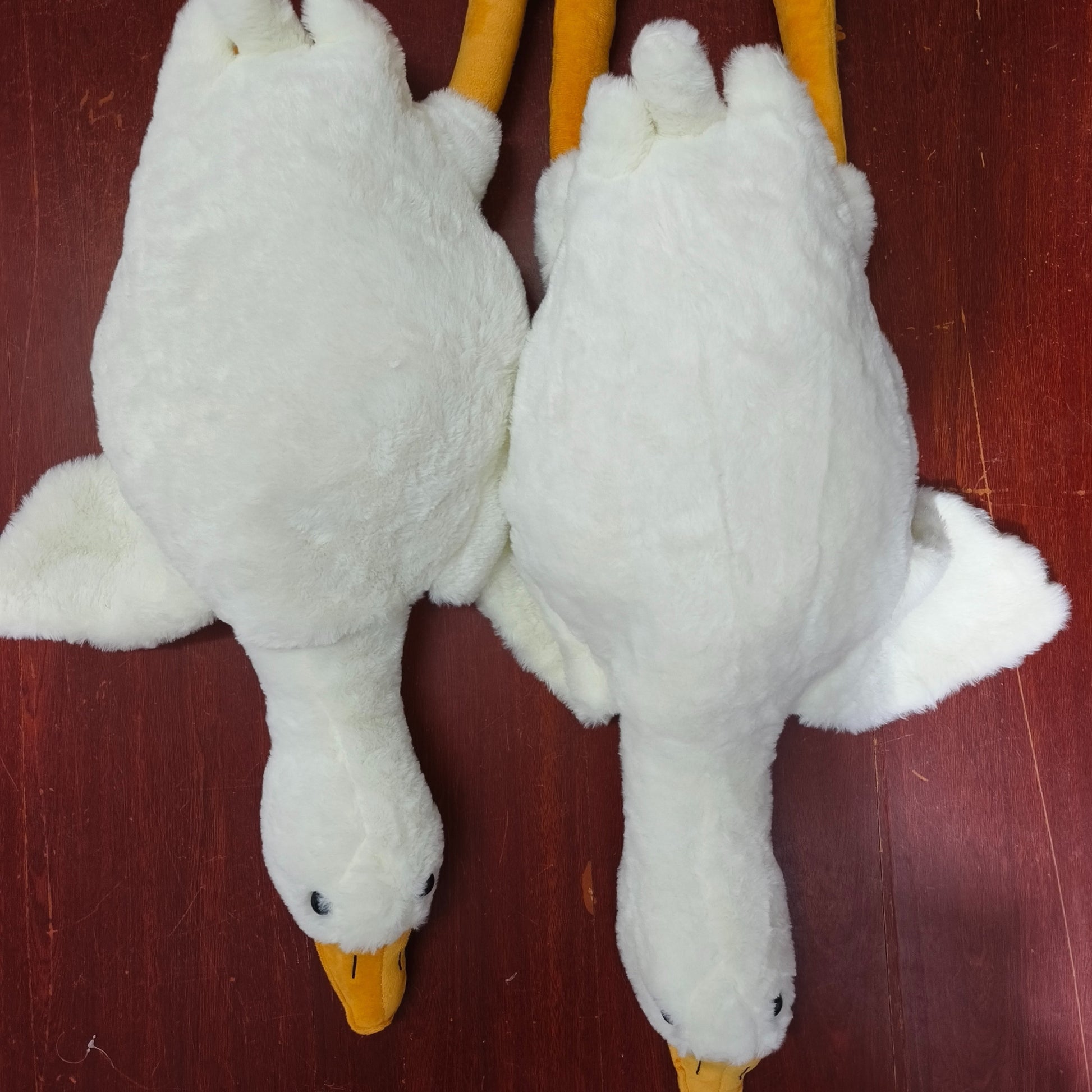 Two white goose plush toy stuffed animals with yellow beaks and legs on a wooden surface